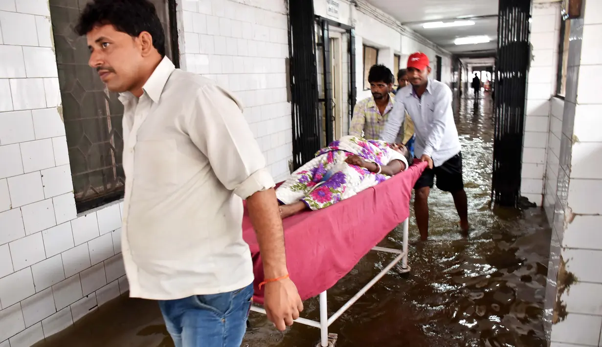 Seorang pasien dipindahkan melewati koridor rumah sakit yang tergenang banjir di Nalanda Medical College Hospital, daerah Bihar, India, 29 Juli 2018. Rumah sakit itu digenangi air kotor dengan sejumlah ikan terlihat berenang memenuhi lantai. (AFP PHOTO)