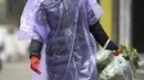 Seorang wanita mengenakan jas hujan  dan masker membawa makanan di Wuhan di provinsi Hubei, China tengah, Senin, (10/2/2020). Angka kematian akibat virus corona di China meningkat lagi, dengan kematian hari Senin (10/2/2020) mencapai 908 orang, dengan adanya 97 kematian baru. (Chinatopix via AP)