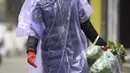 Seorang wanita mengenakan jas hujan dan masker membawa makanan di Wuhan di provinsi Hubei, China tengah, Senin, (10/2/2020). Angka kematian akibat virus corona di China meningkat lagi, dengan kematian hari Senin (10/2/2020) mencapai 908 orang, dengan adanya 97 kematian baru. (Chinatopix via AP)