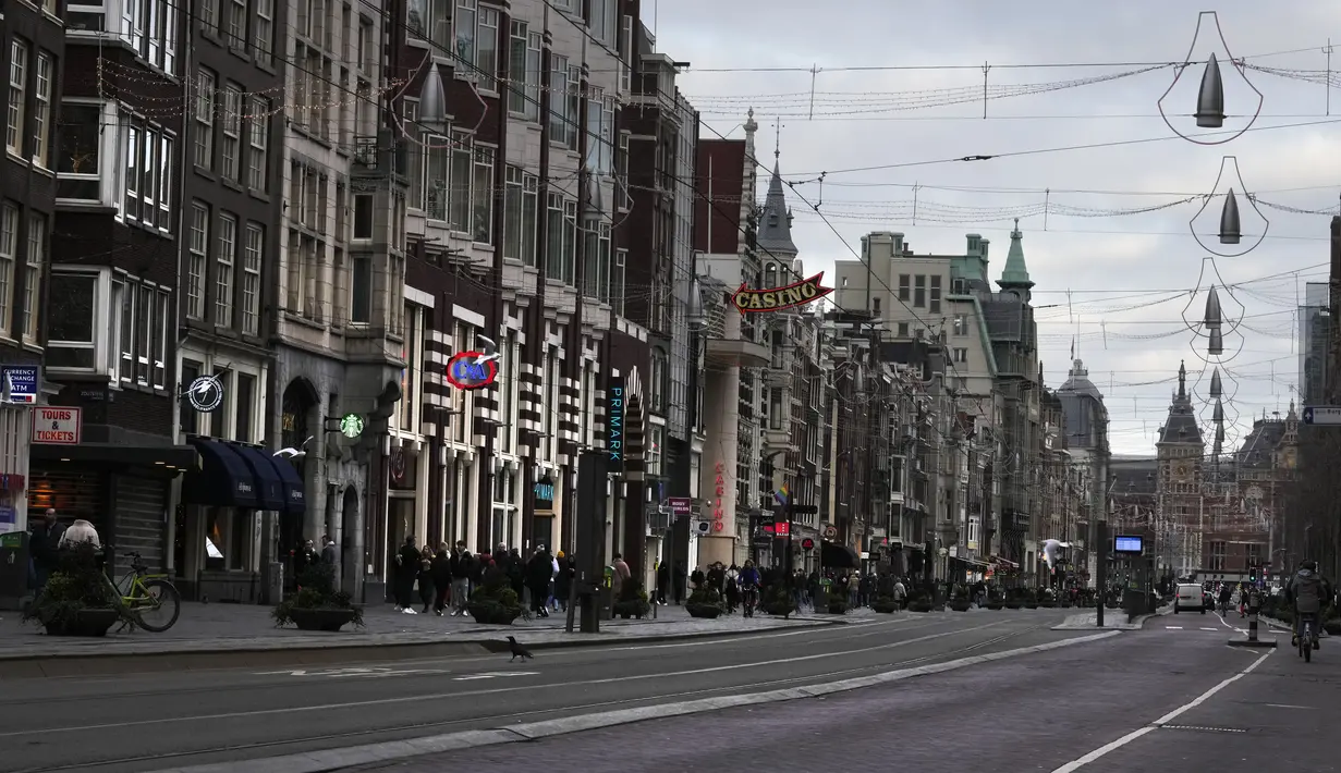 Orang-orang melewati toko-toko yang tutup di jalan perbelanjaan yang biasa ramai di pusat kota Amsterdam, 20 Desember 2021. Negara-negara di Eropa mempertimbangkan pembatasan yang lebih ketat guna membendung gelombang baru infeksi COVID-19 yang didorong oleh varian omicron.  (AP Photo/Peter Dejong)