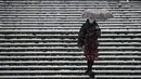 Seorang wanita  mengenakan masker dan payung menuruni tangga yang dipenuhi salju di Universitas Simon Fraser, Burnaby, British Columbia, Kanada (21/12/2020). Peringatan hujan salju yang dikeluarkan masih berlaku untuk beberapa bagian Metro Vancouver. (Darryl Dyck/The Canadian Press via AP)