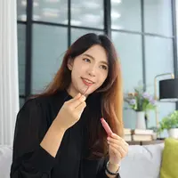 Ilustrasi seorang perempuan sedang memakai lip tint di depan kamera dan ring light.