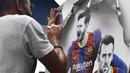 Seorang pekerja melepas poster-poster yang menampilkan pemain depan Barcelona Lionel Messi di stadion Camp Nou di Barcelona (10/8/2021). Prancis menunggu dengan tidak sabar Lionel Messi dengan para pendukung berkumpul di luar lapangan Paris Saint-Germain. (AFP/ Pau Barrena)
