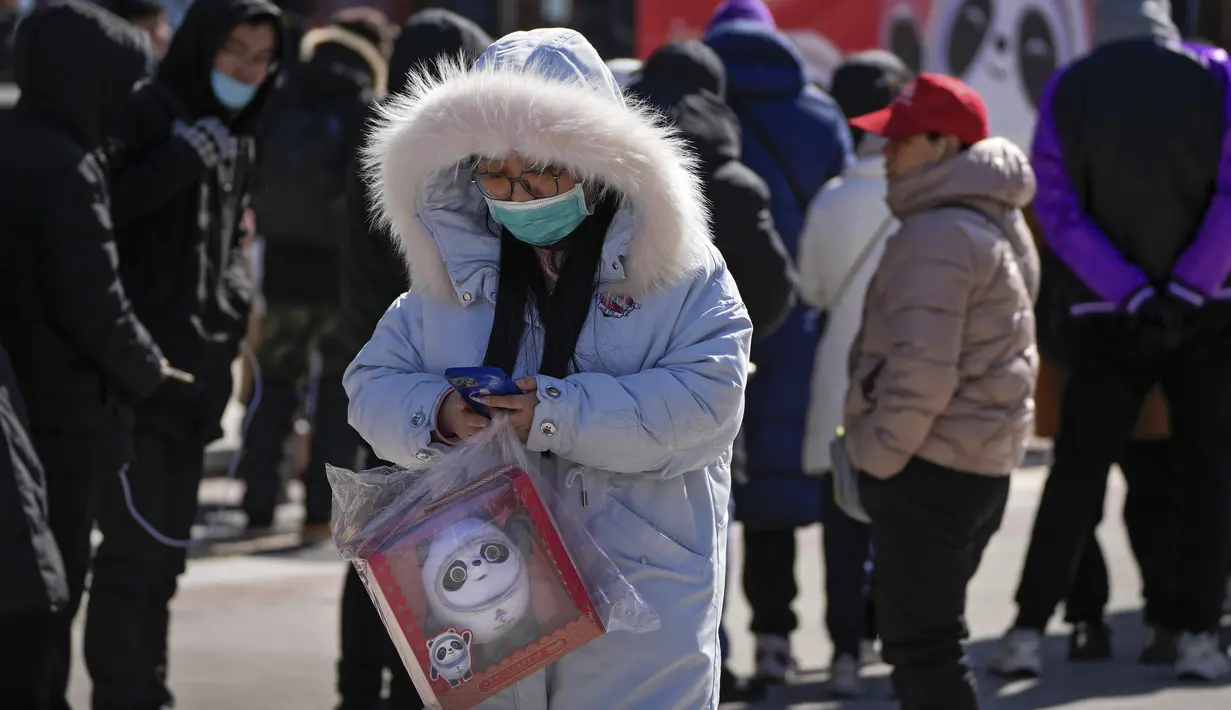 Seorang wanita membawa boneka maskot Olimpiade Bing Dwen Dwen melewati ratusan warga yang berbaris di luar toko yang menjual memorabilia resmi Olimpiade di Beijing, 21 Februari 2022. Boneka maskot Olimpiade masih tetap populer meskipun Olimpiade Musim Dingin telah berakhir. (AP Photo/Andy Wong)