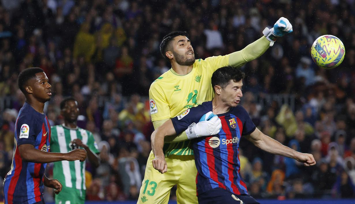 Pemain Barcelona, Robert Lewandowski, berebut bola dengan kiper Real Betis, Rui Silva, pada laga Liga Spanyol di Stadion Camp Nou, Minggu (30/4/2023). (AP Photo/Joan Monfort)