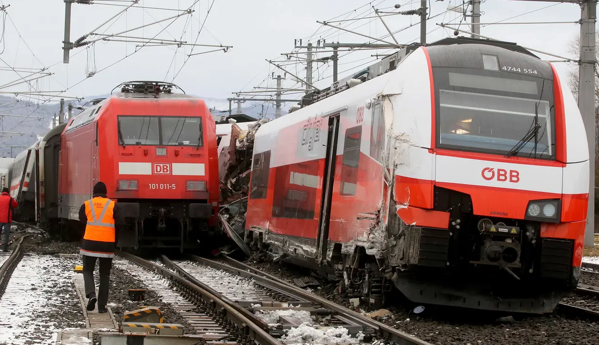 Regu penyelamat berdiri dekat dua rangkaian kereta penumpang yang terlibat tabrakan dekat stasiun di Niklasdorf, Austria, Senin (12/2). Pihak berwenang masih melakukan penyelidikan untuk mengetahui penyebab pasti kecelakaan tersebut. (AP/Ronald Zak)