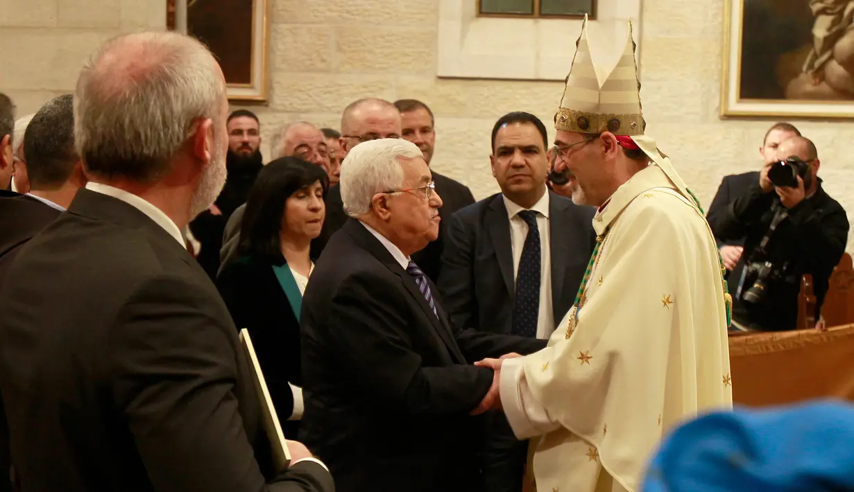 Presiden Palestina Mahmoud Abbas memberikan ucapan selamat Natal pada Uskup Agung Pierbattista Pizzaballa saat misa Natal di Gereja Santa Katarina yang terhubung ke Gereja Nativity, di kota Bethlehem di Tepi Barat, (25/12). (AFP Photo/Musa Shaer Poll)