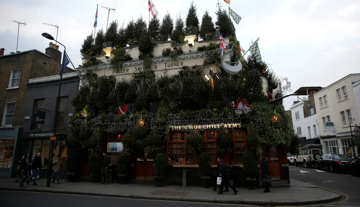 Pejalan kaki melintas di depan bangunan bar The Churchill Arms di London, Inggris, 20 Desember 2016. Pemilik bar tersebut menghabiskan dana sebesar Rp502 juta untuk hiasan pohon natal dan Rp419 juta untuk karangan bunga. (REUTERS/Neil Hall)
