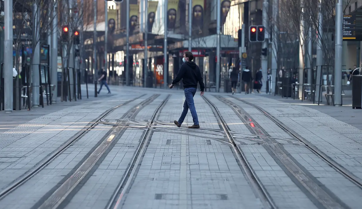 Seorang pria melintasi jalan yang sepi di Sydney (21/8/2021). Kota itu memperpanjang penguncian selama dua bulan dan memberlakukan jam malam sebagian untuk menahan wabah virus corona yang menyebar cepat. (AFP/David Gray)