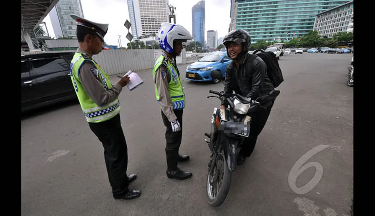 Petugas kepolisian menilang seorang pengendara motor yang menerobos Jalan MH Thamrin, Jakarta, Minggu (18/1/2015). (Liputan6.com/Miftahul Hayat)