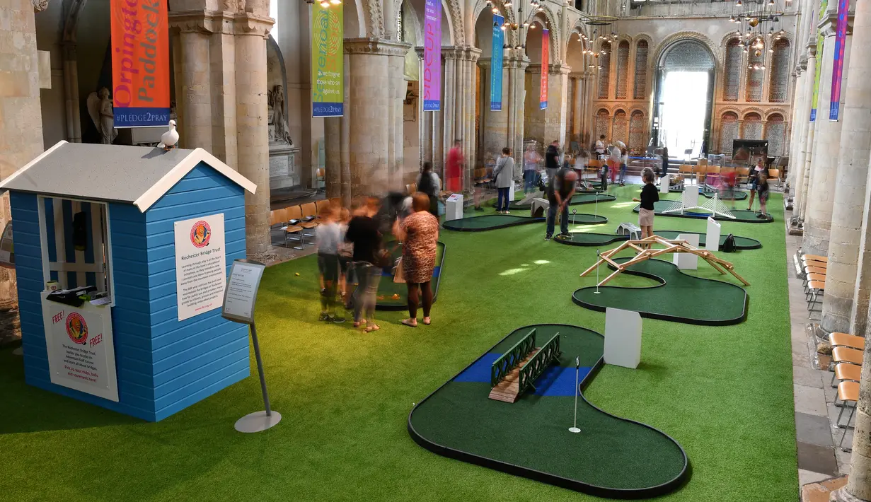 Orang-orang bermain di lapangan golf kecil yang didirikan  di dalam Katedral Rochester, Inggris pada 6 Agustus 2019. Lapangan golf ini membentang di sepanjang lorong dan memiliki sembilan lubang dengan miniatur jembatan.  (Ben STANSALL / AFP)