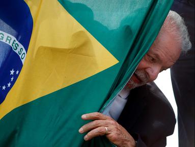 Mantan presiden Brasil (2003-2010) dan kandidat presiden dari Partai Pekerja (PT) berhaluan kiri, Luiz Inacio Lula da Silva, muncul di belakang bendera nasional Brasil selama kampanye di Sao Mateus, Negara Bagian Sao Paulo, Brasil, Senin (17/10/2022). Lula da Silva dan presiden Jair Bolsonaro akan menghadapi putaran kedua pemilihan presiden pada 30 Oktober, dengan ekspektasi persaingan ketat mendorong kedua belah pihak untuk mengintensifkan kampanye pemilihan. (Miguel SCHINCARIOL / AFP)