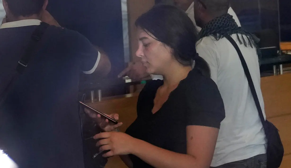 Sali Hafez (tengah) ditemani oleh para aktivis melihat teleponnya setelah aksi membobol cabang Bank BLOM, Beirut, Lebanon, Rabu (14/9/2022). Lebanon telah dihantam oleh krisis ekonomi terburuk sejak 2019. (AP Photo/Hussein Malla)