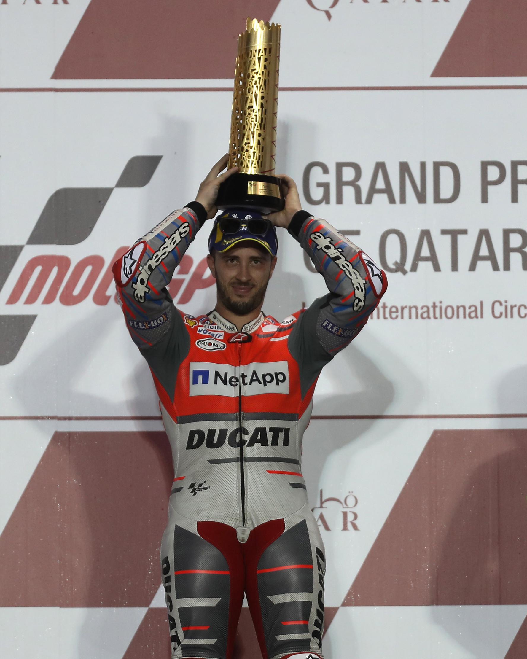 Pembalap Ducati Andrea Dovizioso berpose diatas podium sambil memegang pialanya usai memenangkan balapan di MotoGP Qatar 2018 di Sirkuit Internasional Losail (18/3). (AFP Photo/Karim Jaafar)