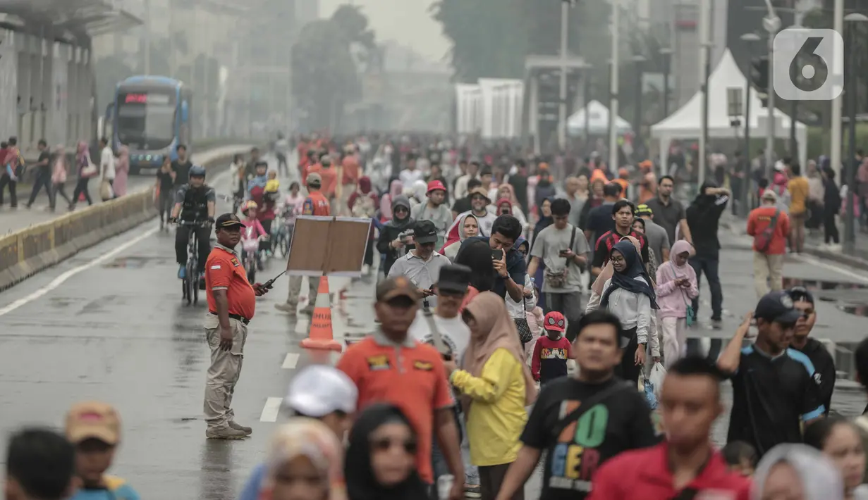 Petugas keamanan berjaga saat warga beraktivitas di car free day (CFD) kawasan Bundaran HI, Jakarta, Minggu (29/12/2019). Kendati tidak seramai saat cerah, warga yang berlari, jalan santai, atau swafoto masih menjadi pemandangan di area CFD usai hujan mengguyur Jakarta. (Liputan6.com/Faizal Fanani)