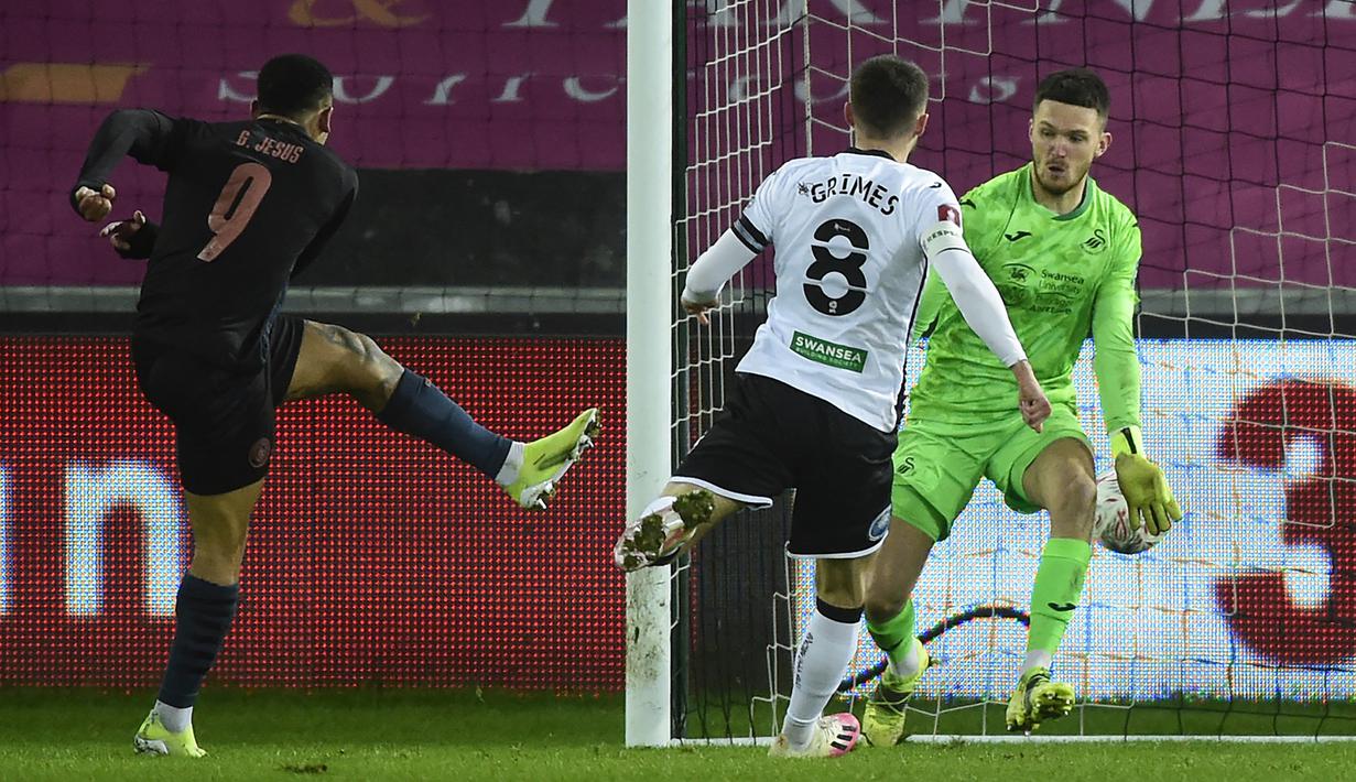 Striker Manchester City, Gabriel Jesus (kiri) melepaskan tendangan yang berbuah gol ketiga timnya ke gawang Swansea City dalam laga babak kelima Piala FA 2020/21 di Liberty Stadium, Rabu (10/2/2021). Manchester City menang 3-1 atas Swansea City. (AFP/Rebecca Naden/Pool)