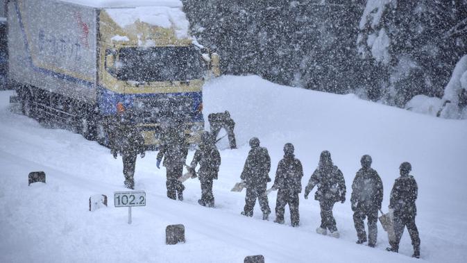 Personel Pasukan Bela Diri Darat menyingkirkan salju di Jalan Tol Hokuriku di Fukui, Jepang, di mana mobil-mobil terus terjebak akibat hujan salju lebat Minggu (10/1/2021). (Kyodo News via AP)