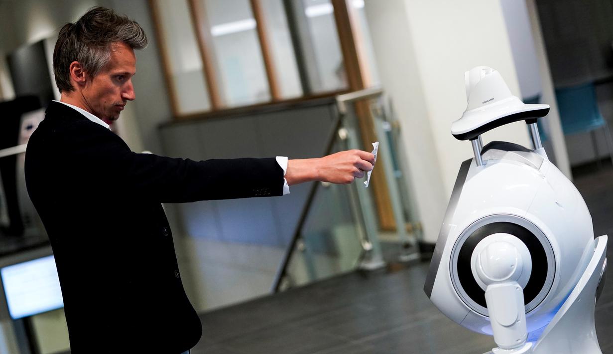 Seorang karyawan perusahaan Belgia, ZoraBots, memperlihatkan kode QR selama pengujian robot yang disebut CRUZR di Antwerp University Hospital (UZA) pada 29 Mei 2020. Robot ini dapat mendeteksi demam serta mengetahui pengunjung rumah sakit  yang memakai Masker atau tidak. (Kenzo TRIBOUILLARD/AFP)