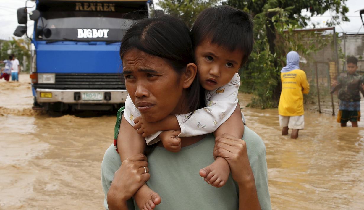 Seorang Perempuan menggendong anaknya melewati jalanan banjir di Nueva Ecija,  Filipina, Senin (19/10/2015). Topan yang memiliki kecepatan angin 175 kilometer per jam ini telah menciptakan gelombang ombak setinggi empat meter. (REUTERS/Erik De Castro)