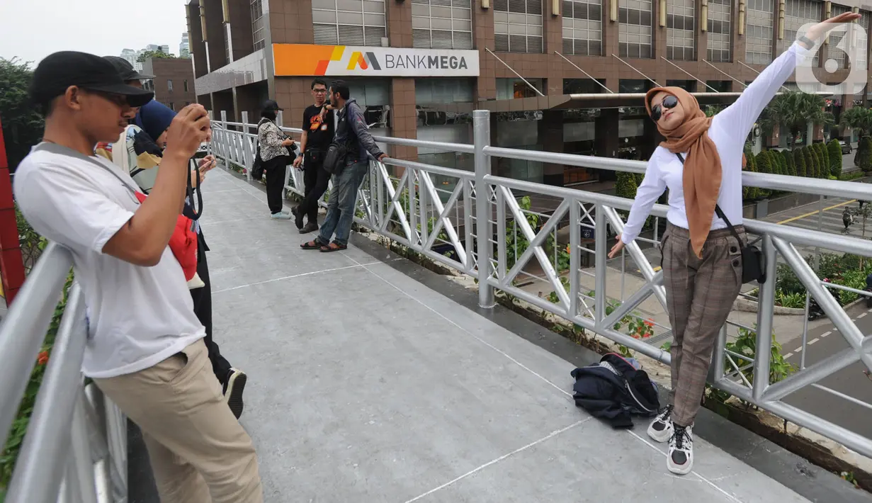 Warga berfoto di jembatan penyeberangan orang (JPO) yang tidak beratap di jalan Sudirman, Jakarta, Rabu (6/11/2019). Pemprov DKI mengklaim mayoritas masyarakat Jakarta setuju dengan konsep JPO terbuka dan tanpa atap yang kini dibangun di Sudirman. (merdeka.com/Arie Basuki)