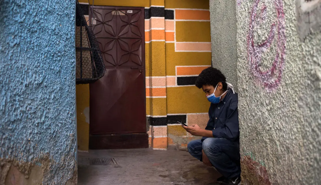 Jonathan Figueroa, 14, menggunakan ponselnya untuk terhubung ke sinyal wifi tetangga, di luar rumahnya, saat sang ibu Viviana Rodriguez mengawasinya di tengah pandemi virus corona di Bello Campo di Chacao, Caracas, Venezuela pada 6 Oktober 2020. (Cristian Hernandez/AFP)