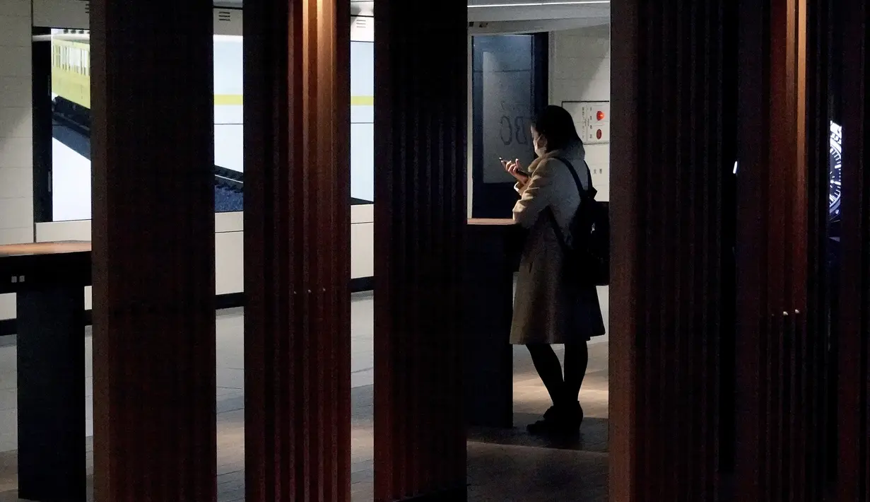 Seorang wanita yang mengenakan masker pelindung untuk membantu mengekang penyebaran virus corona terlihat di sebuah tempat ponsel di Tokyo (19/1/2021). Ibukota Jepang itu mengonfirmasi lebih dari 1.200 kasus Virus Corona baru pada 19 Januari 2021. (AP Photo/Eugene Hoshiko)