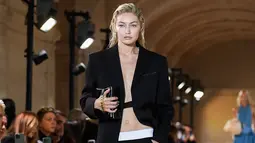 Model AS Gigi Hadid mempersembahkan kreasi untuk peragaan busana Victoria Beckham Spring-Summer 2023 pada Paris Womenswear Fashion Week di Paris, Prancis, 30 September 2022. Penampilan Gigi kian menawan dilengkapi sepasang celana panjang hitam dengan ikat pinggang putih tebal serta tali yang digantung pada jaket bergaya. (JULIEN DE ROSA/AFP)