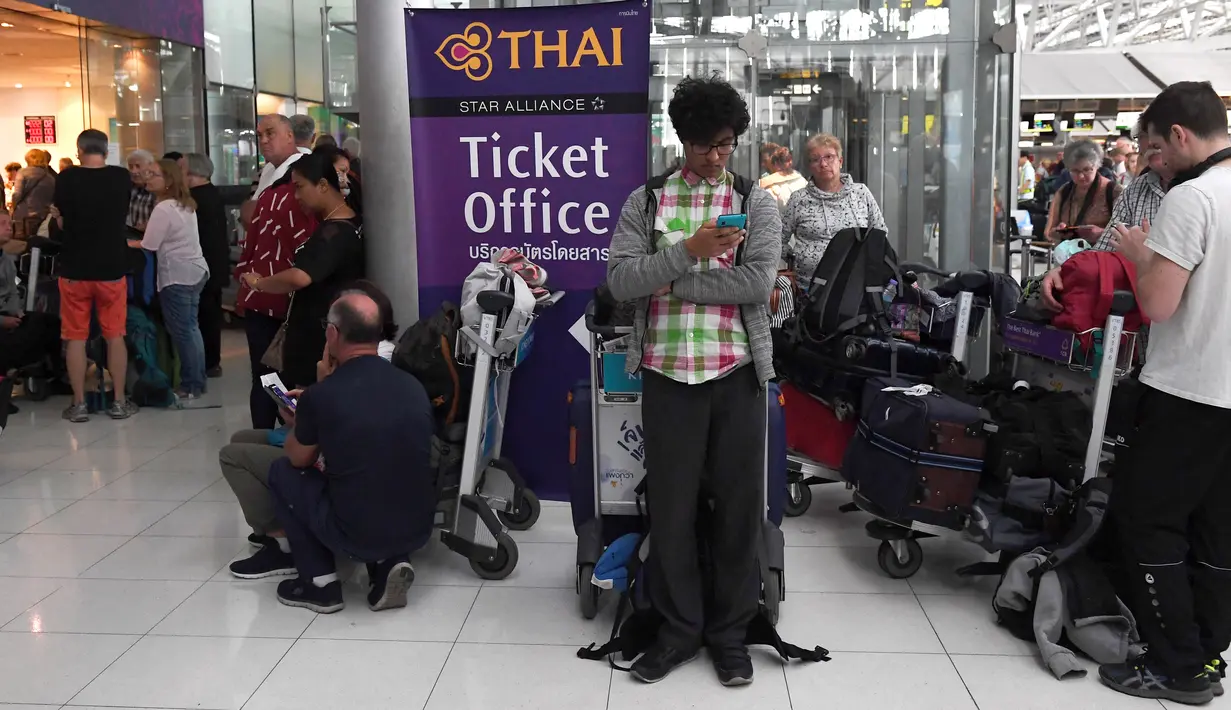 Seorang penumpang bermain ponsel di deka tloket tiket Thai Airways di Bandara Internasional Suvarnabhumi di Bangkok (28/2). Hampir Ribuan penumpang tujuan Pakistan dan Eropa terjebak di bandara tersebut. (AFP Photo/Lillian Suwnrumpha)