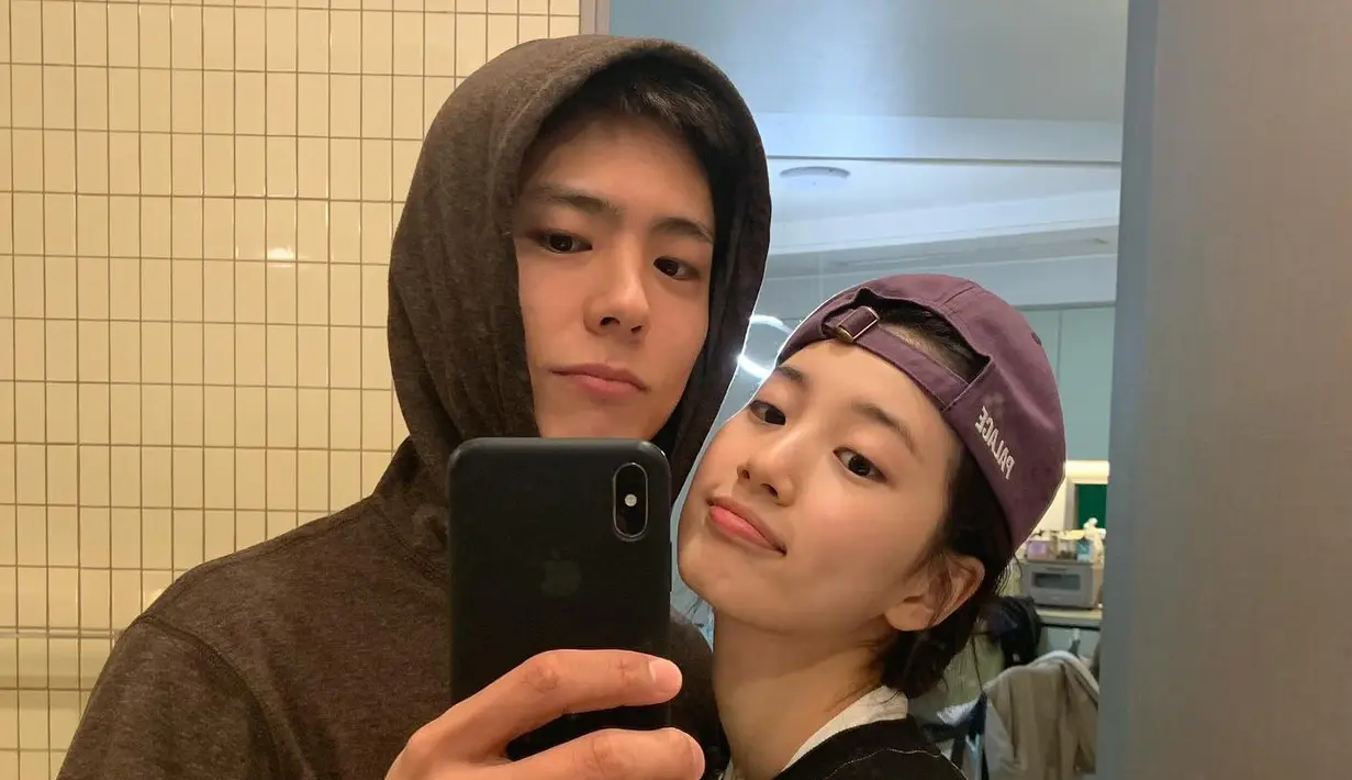 <p>Suzy dan Park Bo Gum melakukan mirror selfie. Bo Gum mengenakan hoodie sementara Suzy berpenampilan boyish dengan hoodie dan topi.</p>