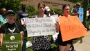 Sejumlah orang membawa poster sambil berdiri di luar Kebun Binatang Cincinnati, Ohio, Senin (30/5). Publik AS marah atas insiden penembakan gorila bernama Harambe untuk menyelamatkan seorang bocah yang jatuh ke kandangnya. (REUTERS/William Philpott)