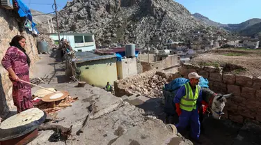 Seorang perempuan membuat roti pipih saat pekerja kota tiba dengan seekor keledai untuk mengumpulkan sampah rumah tangga di kota Akre, sekitar 500 km sebelah utara Baghdad, Irak, 13 Februari 2021. Pemerintah kota Akre menggunakan keledai dan anak kuda untuk mengumpulkan sampah. (SAFIN HAMED/AFP)