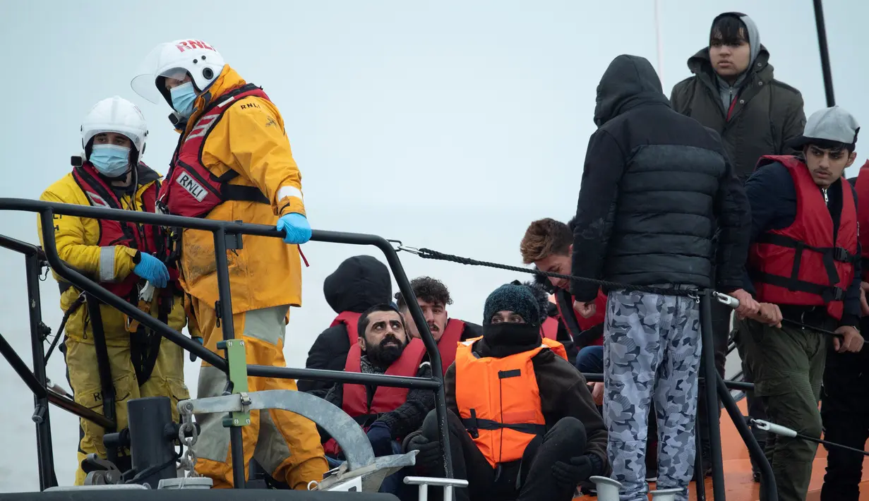 Para migran duduk di atas sekoci RNLI (Royal National Lifeboat Institution) setelah diselamatkan saat menyeberangi Selat Inggris di lepas pantai di Dungeness, Inggris tenggara (24/11/2021). (AFP/Ben Stansall)