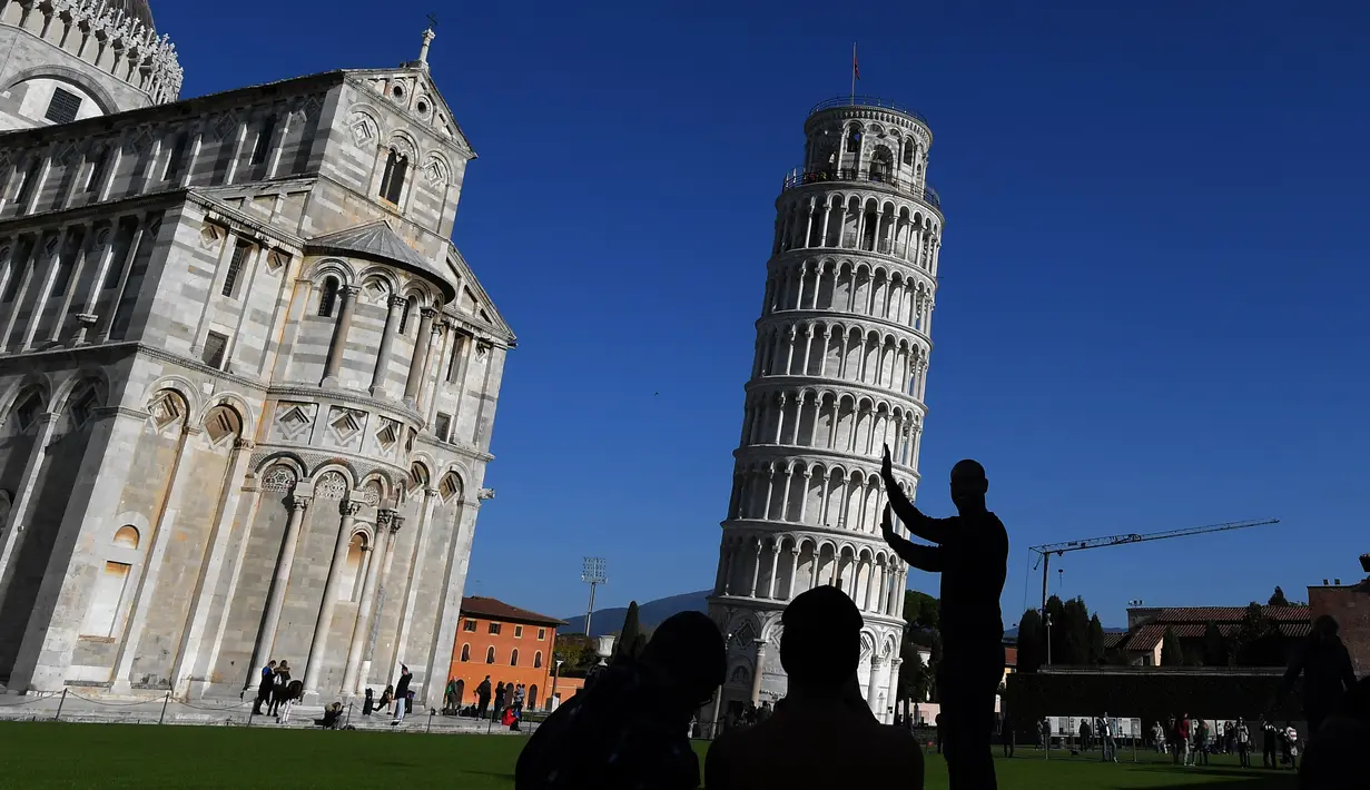Turis berpose di depan Menara Pisa di kota Pisa, Italia pada 28 November 2018. Kemiringan Menara Pisa yang tersohor kini telah stabil setelah sedikit diluruskan dalam upaya menyelamatkan situs pariwisata ternama dunia itu. (Tiziana FABI / AFP)