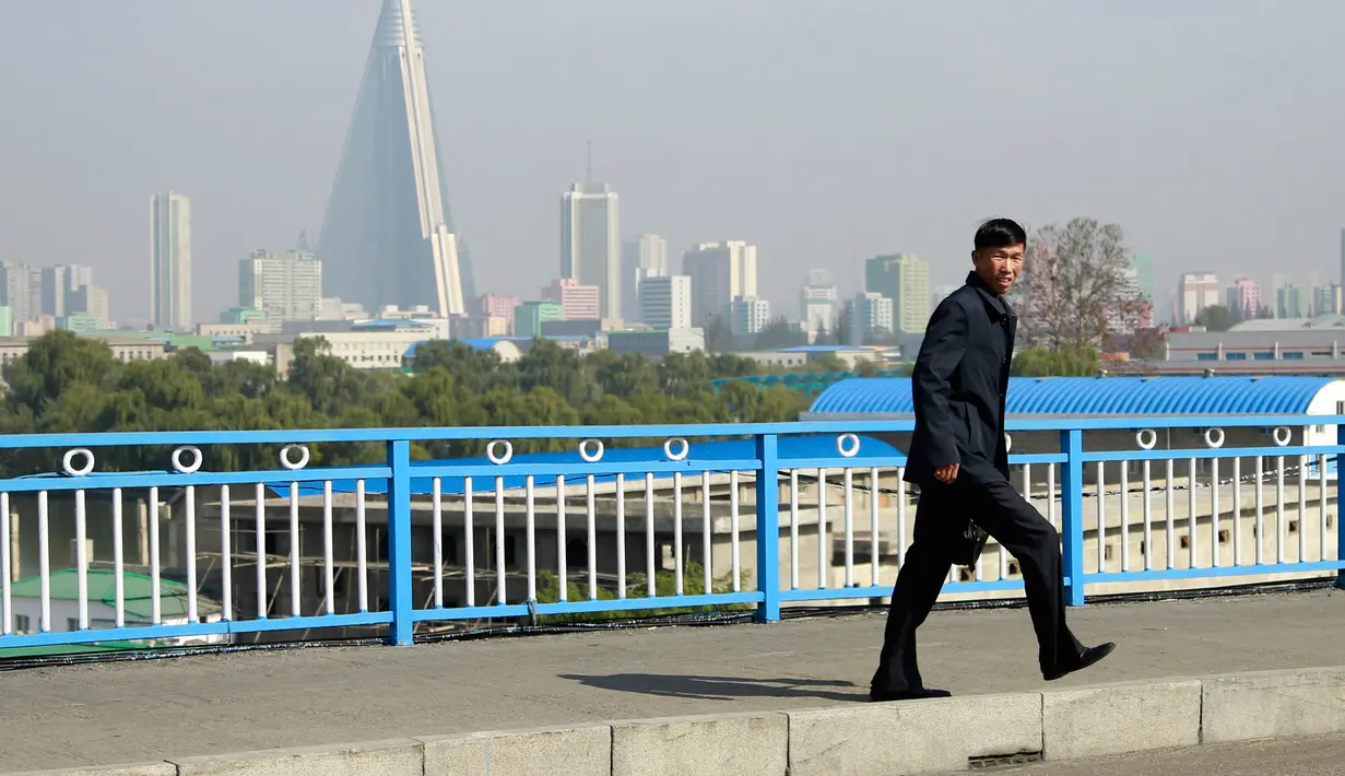 Seorang pria berjalan di jembatan dengan latar Ryugyong Hotel berbentuk piramida terlihat di Pyongyang, Korea Utara, (21/10). (AP Photo / Dita Alangkara)
