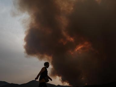Seorang wanita berjalan saat asap dari kebakaran hutan memenuhi langit di Uiseong, Korea Selatan pada tanggal 24 Maret 2025. (YASUYOSHI CHIBA/AFP)