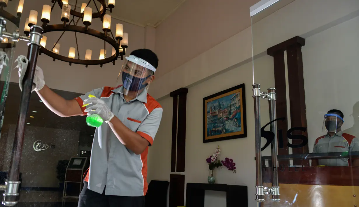 Seorang pekerja dengan mengenakan alat pelindung membersihkan pintu sebuah hotel yang dibuka kembali setelah penutupan selama ditutup selama tiga bulan akibat pandemi COVID-19 di Banda Aceh pada Rabu (15/7/2020). (Photo by CHAIDEER MAHYUDDIN / AFP)