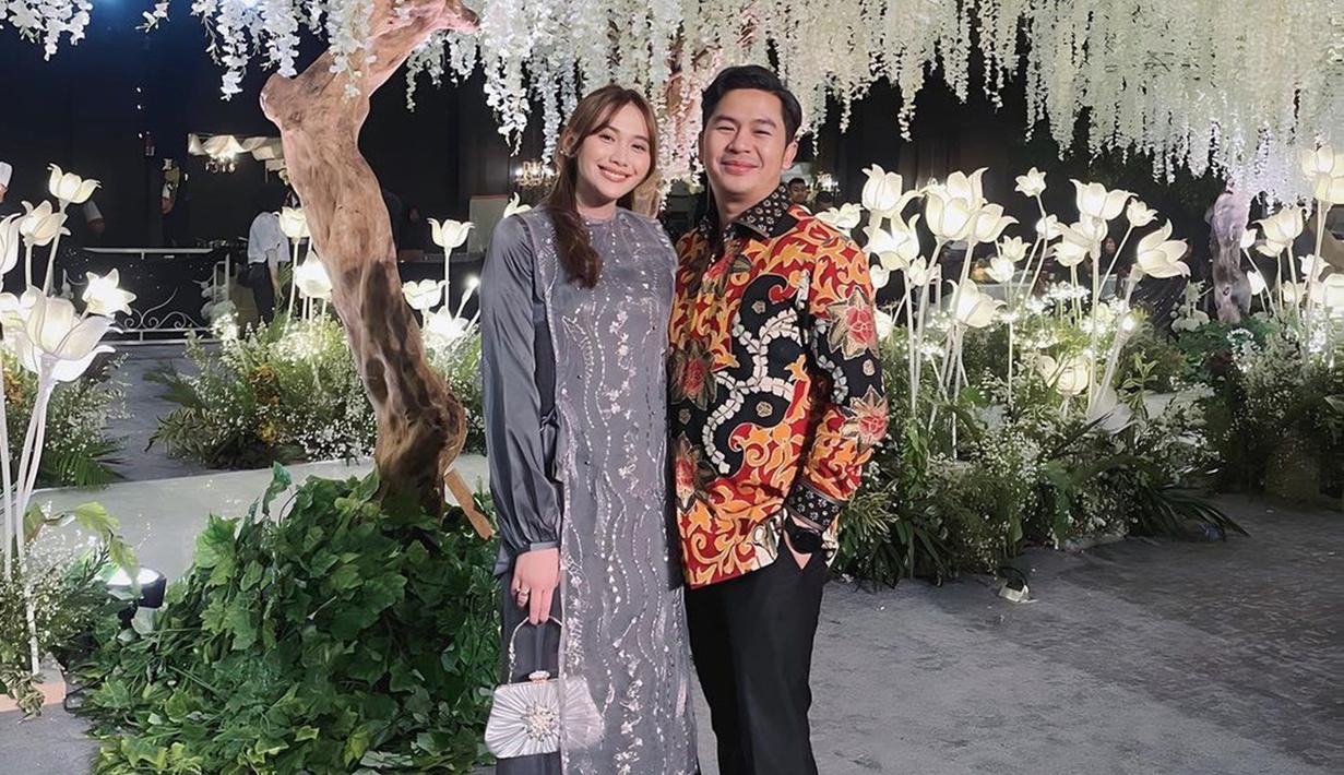 Ini adalah foto manis Marsha Risdasari dan sang suami di resepsi pernikahan Adiba dan Egy. Marsha tampil cantik dengan dress simpel warna abu-abu, sementara sang suami gagah dengan baju batik. Tatanan rambut ikat tengah membuat Marsha jadi makin cantik. Meski sudah menikah dan jadi ibu, namun tak dipungkiri jika artis kelahiran 1998 ini masih terlihat bak ABG. (Liputan6.com/IG/@marshariss)