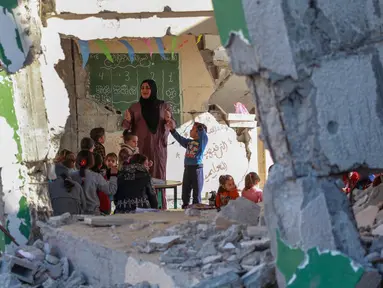 Foto yang dipublikasikan pada 4 Desember 2024 menunjukkan seorang guru Palestina, Doha al-Attar (30) saat memberi pelajaran kepada anak-anak di sebuah ruang kelas yang rusak parah di Khan Yunis, wilayah selatan Jalur Gaza. (Bashar TALEB/AFP)