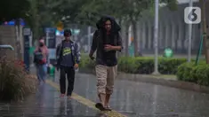 Warga menutupi kepala dari guyuran hujan saat melintasi kawasan Sudirman, Jakarta, Kamis (4/1/2024). (Liputan6.com/Angga Yuniar)