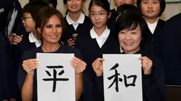 Melania Trump (kiri) dan Istri PM Jepang, Akie Abe menunjukkan huruf kanji yang berarti "Damai" saat menghadiri kelas kaligrafi di sekolah dasar Kyobashi Tsukiji, Tokyo (6/11). (AFP Photo/Pool/Toshifumi Kitamura)