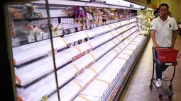 Seorang pembeli berjalan melewati rak kosong di sebuah toko di Tokyo, Jumat (11/10/2019). Banyak toko-toko perbelanjaan di Jepang yang kehabisan makanan dan minuman akibat warganya yang menimbun makanan untuk menghadapi topan Hagibis. (Franck FIFE / AFP)