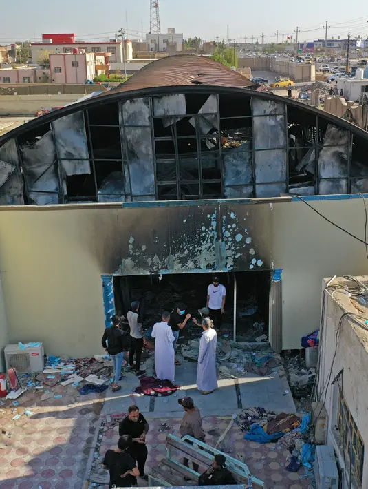 Foto udara menunjukkan orang-orang melihat-lihat bangsal isolasi virus corona yang porak-poranda di rumah sakit Al-Hussein setelah kebakaran, di kota Nasiriyah, Irak selatan, Selasa (13/7/2021). Tragedi yang terjadi Senin malam ini diduga dipicu oleh ledakan tangki oksigen. (Asaad NIAZI/AFP)