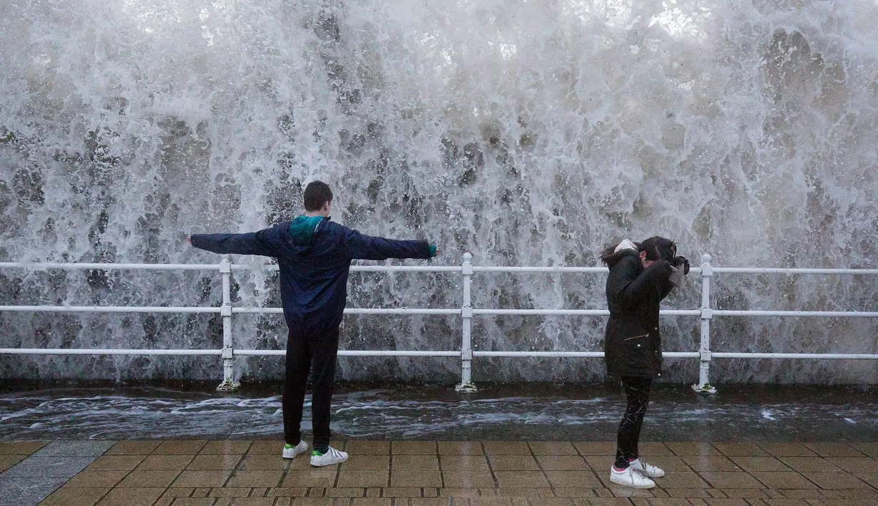 Anak-anak berdiri saat ombak besar yang disebabkan badai Eleanor di atas dinding laut di Aberystwyth di barat Wales (3/1). Badai Eleanor membawa angin hingga 100 mph. (Aaron Chown / PA via AP)