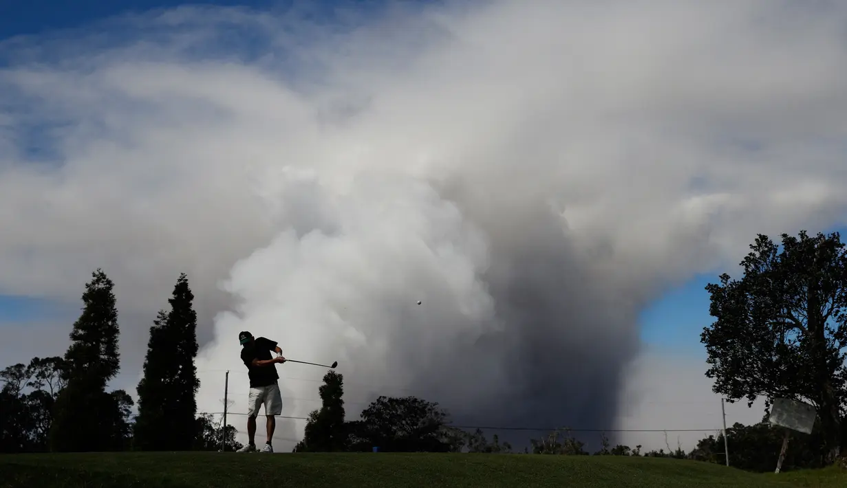 Mike Walls bermain golf saat kepulan asap abu vulkanik berembus dari puncak gunung Kiluaea di Volcano, Hawaii (21/5). Gunung Kilauea mulai meletus pada 3 Mei yang membuat sekitar 40 bangunan hangus terbakar. (AP Photo/Jae C. Hong)