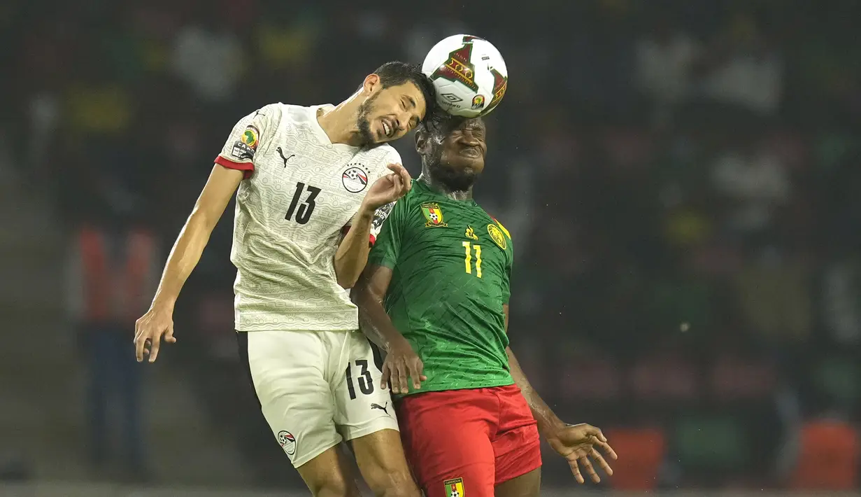 Bek Mesir, Ahmed Fatouh melompat saat berebut bola dengan penyerang Kamerun Christian Bassogog pada laga semifinal Piala Afrika 2021 di Paul Biya Stadium, Jumat (4/2/2022) dini hari WIB. Mesir sukses mengalahkan Kamerun 3-1 via drama adu penalti. (AP Photo/Themba Hadebe)