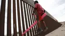 Seorang anak bermain jungkat-jungkit yang dipasang di antara pagar pemisah Meksiko dengan Amerika Serikat, Ciudad de Juarez, Meksiko, Minggu (28/7/2019). Jungkat-jungkit tersebut dirancang seorang profesor arsitektur California, Ronald Rael. (AP Photo/Christian Chavez)