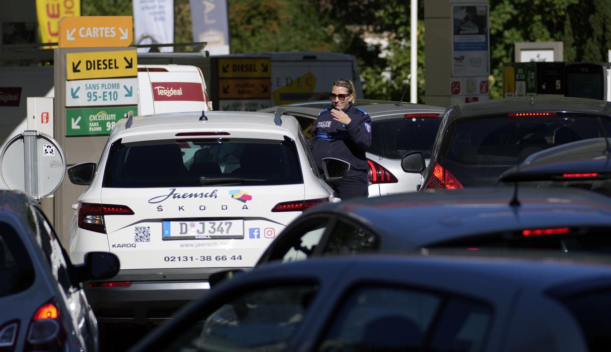 Seorang petugas polisi mengarahkan mobil saat pengemudi berbaris di sebuah pompa bensin di Paris, Selasa (11/10/2022). Untuk mengatasi kelangkaan bahan bakar, pemerintah Prancis telah merilis volume BBM yang signifikan dari stok strategisnya dan mengintensifkan impor BBM dari Belgia. (AP Photo/Christophe Ena)