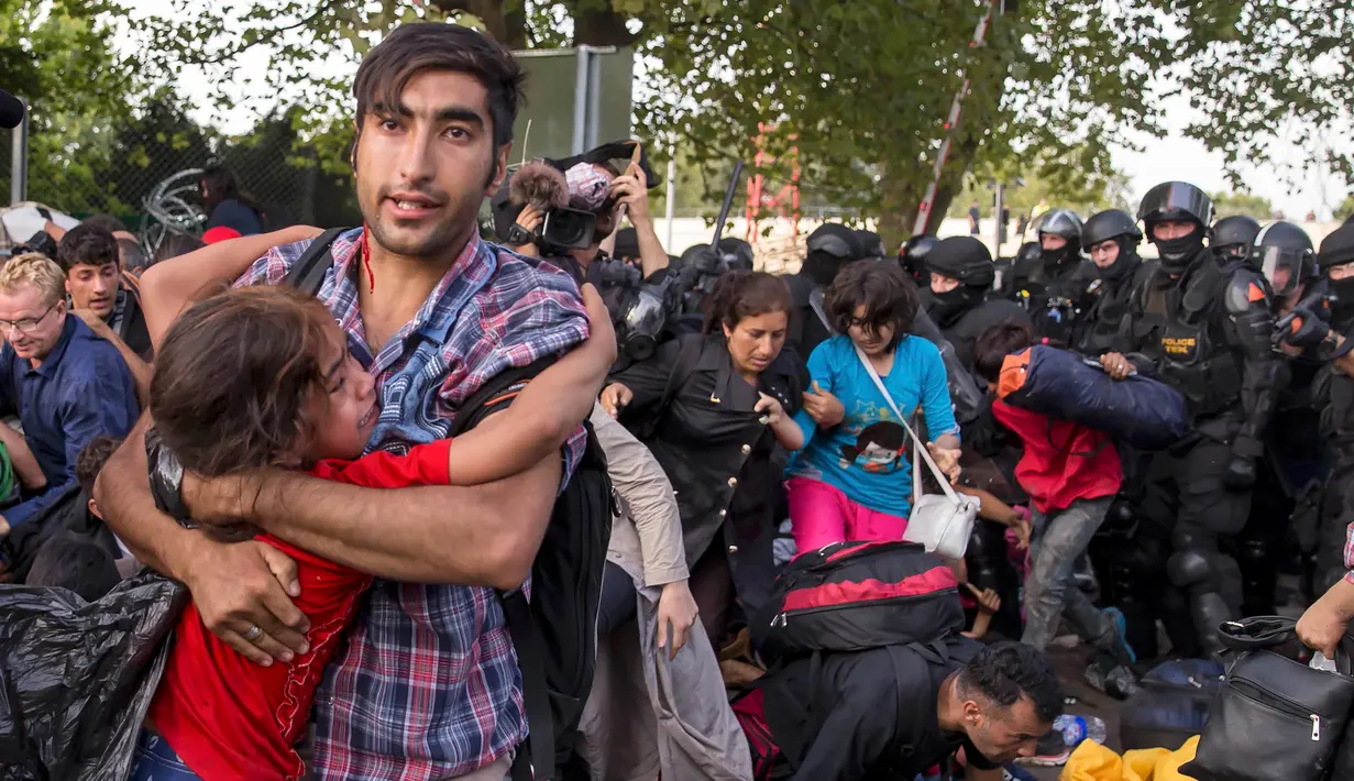 Seorang imigran menyelamatkan diri sambil menggendong anaknya di tengah bentrokan polisi dengan imigran yang berusaha menerobos pintu perbatasan antara Serbia dan Hungaria di Roszke, Rabu (16/9/2015). (REUTERS/Marko Djurica)