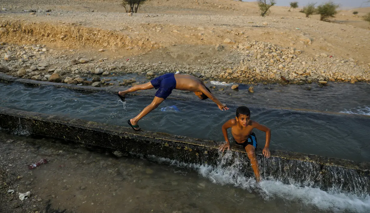 Anak-anak bermain di aliran mata air yang digunakan untuk irigasi untuk mendinginkan tubuh saat suhu udara mencapai 44 derajat Celcius di kota Jericho, Tepi Barat (1/9/2020). (AFP Photo/Ahmad Gharabli)