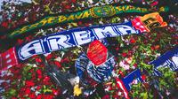 Syal Arema FC dan Persebaya Surabaya diletakkan di atas tumpukan bunga duka cita di Stadion Kanjuruhan, Kabupaten Malang, Jumat (7/7/2022). (Bola.com/Bagaskara Lazuardi)